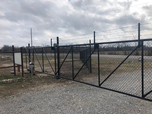A chain link fence with barbed wire surrounding a gravel road.