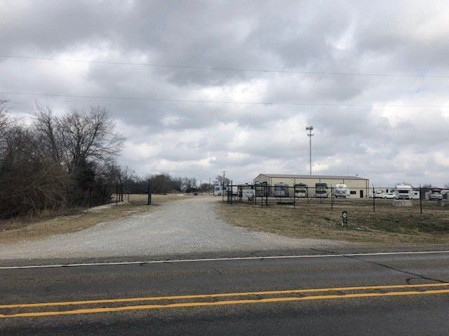 A dirt road going through a field with a building in the background.