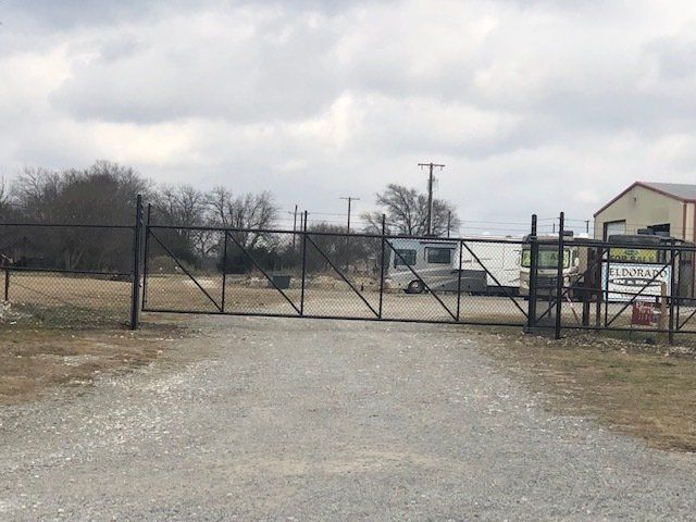 A fence surrounds a gravel road with a building in the background.