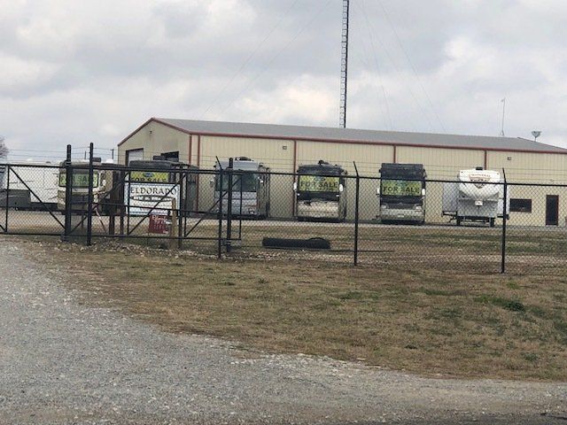 Several rvs are parked in front of a building behind a fence.