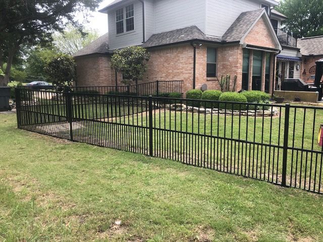 A black metal fence is in front of a brick house.