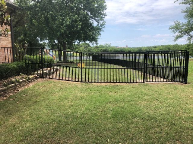 A black metal fence surrounds a large lush green field.