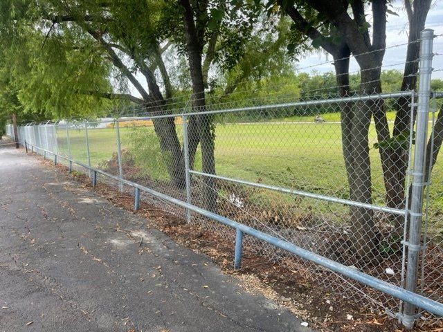 A chain link fence surrounds a field with trees in the background.