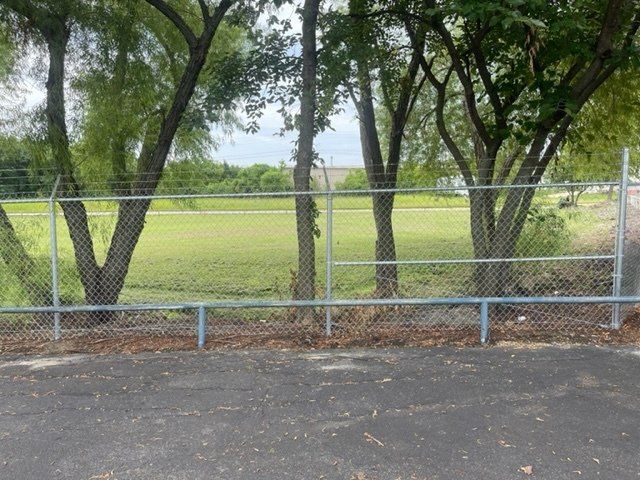 A chain link fence surrounds a field with trees in the background