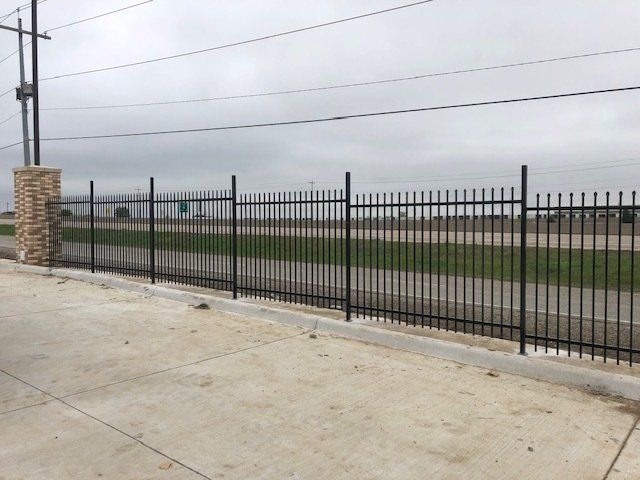A black metal fence is surrounding a grassy field.