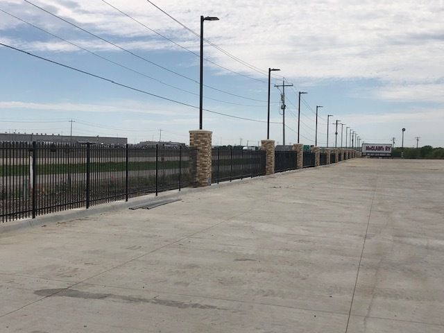 A concrete walkway with a fence and power lines in the background