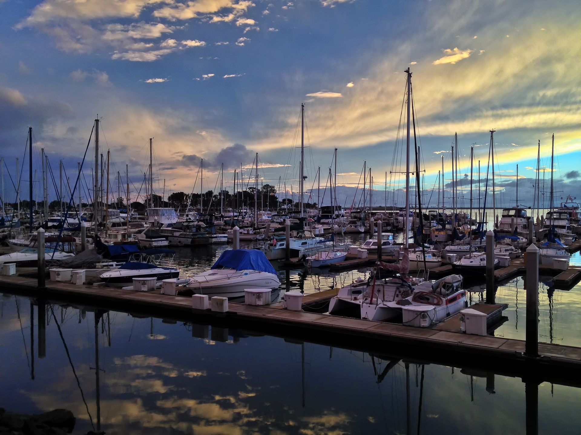 Many boats are docked in a marina at sunset