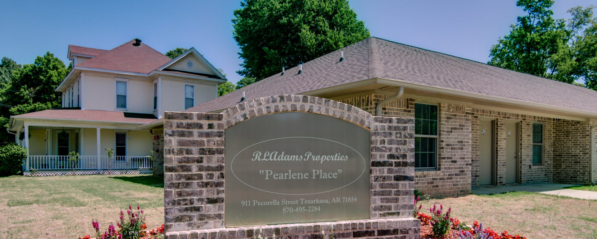 Stone sign for Alexandria House at a red-brick, historic-style building with a porch and trees behind it