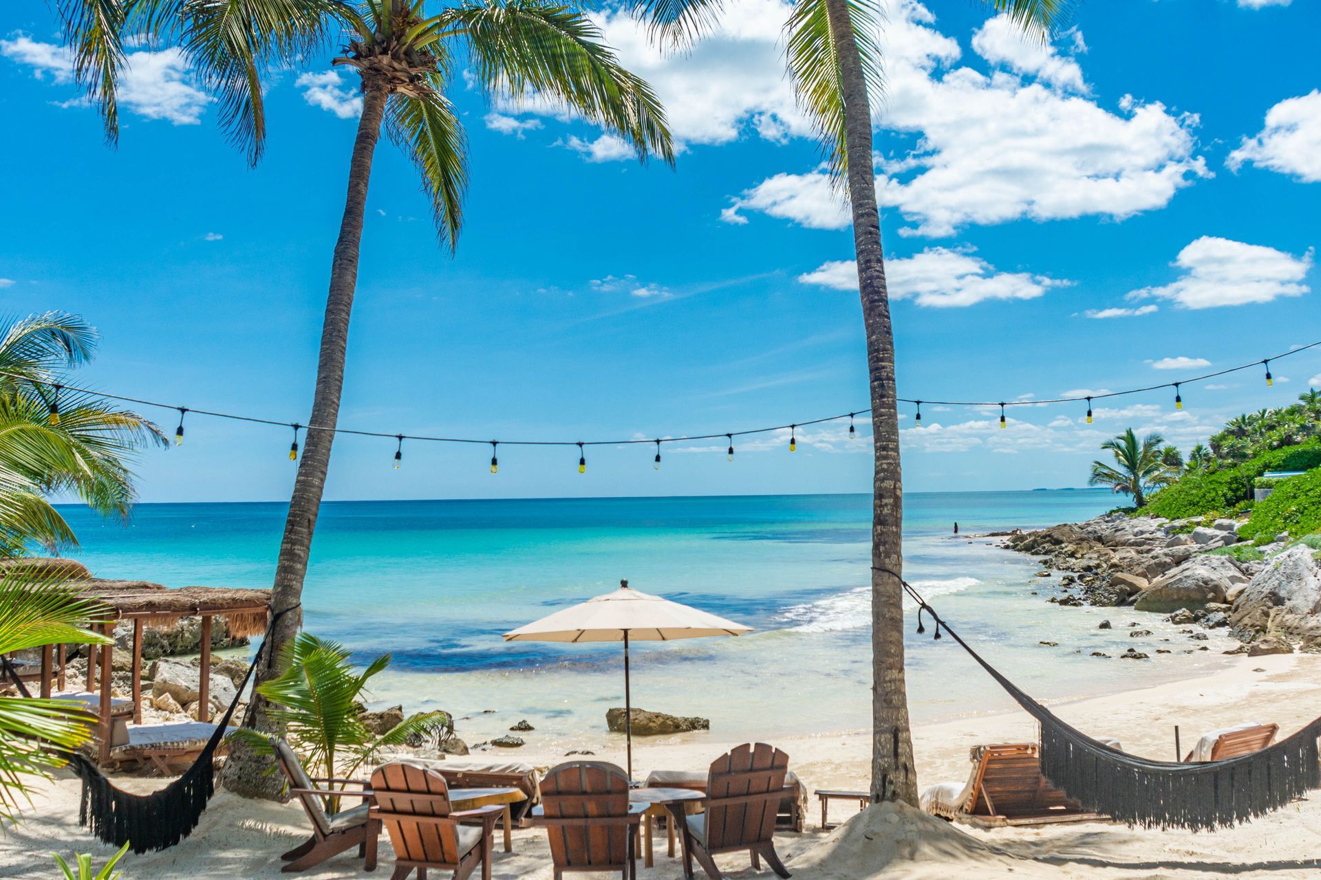 A beach with palm trees , chairs , umbrellas and hammocks.