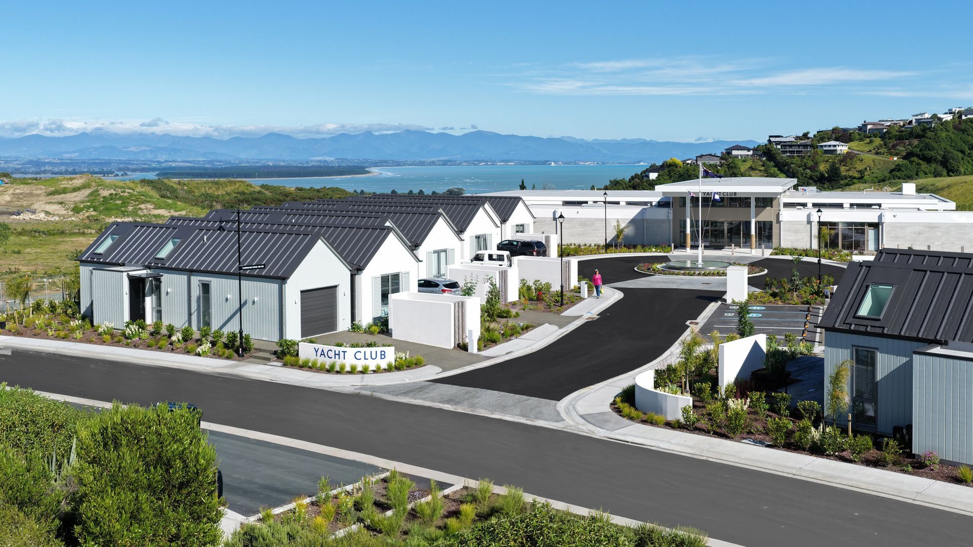 Modern white houses and apartments in a sunny coastal neighborhood with hills and blue sky