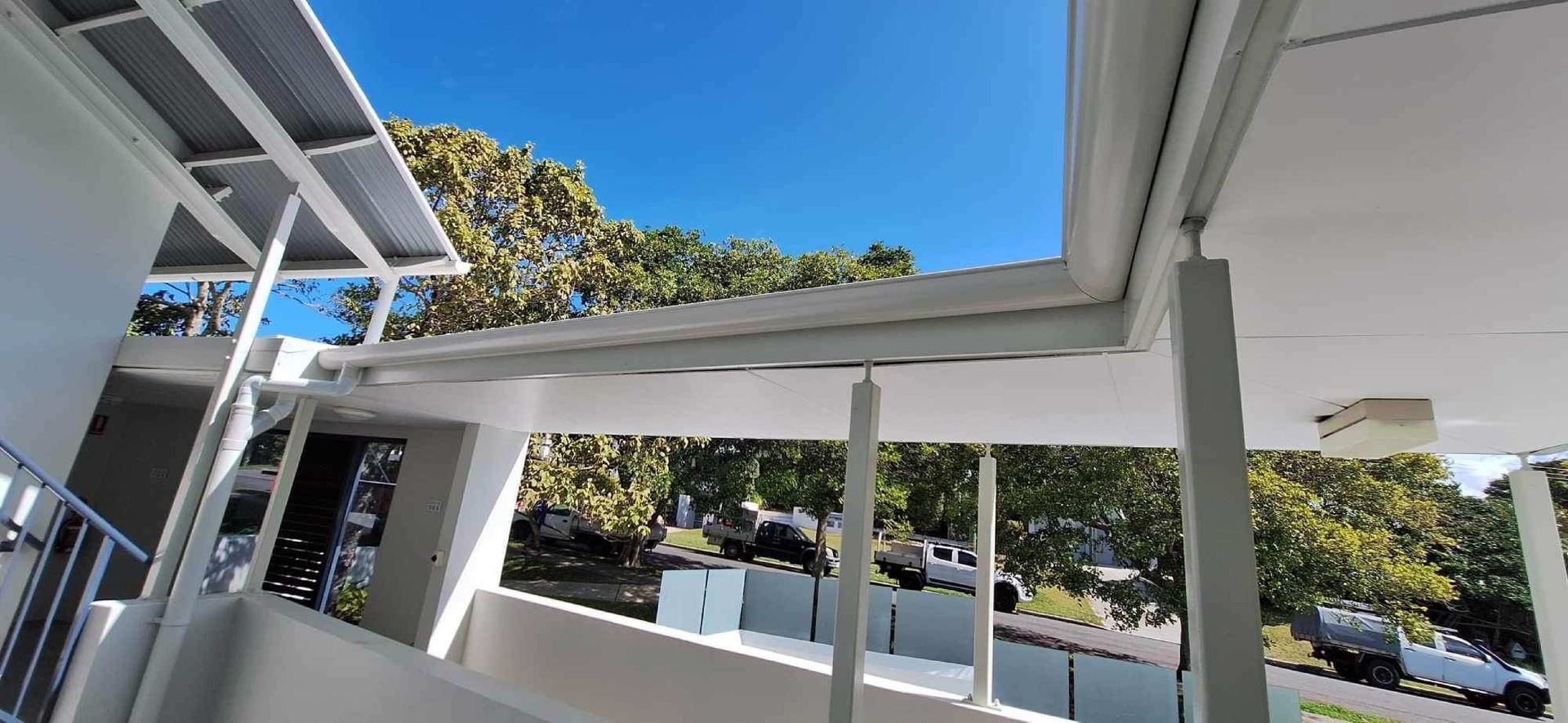 A Man Is Installing A White Gutter On The Side Of A House — Coastal Roof & Gutter Services In Coolum Beach, QLD