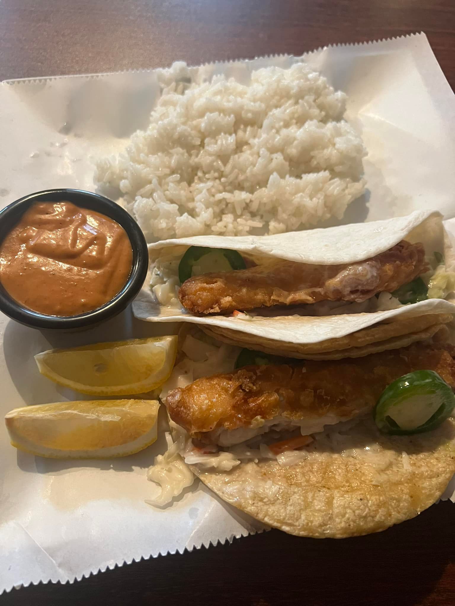 A close up of a fish taco with rice and sauce on a table.