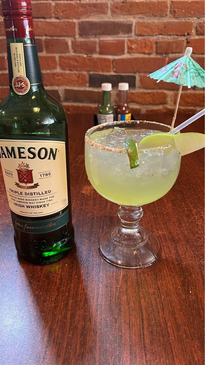 A bottle of jameson next to a margarita on a table.