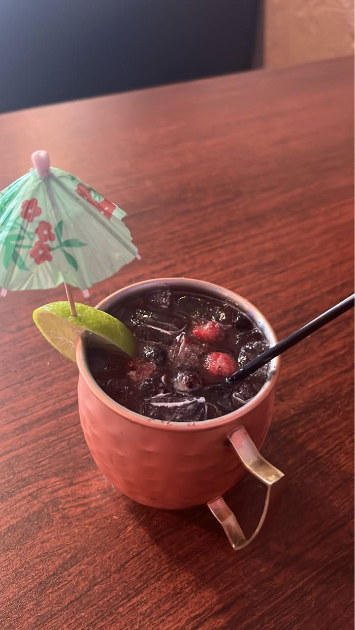 A cup of drink with straws and an umbrella on a wooden table.