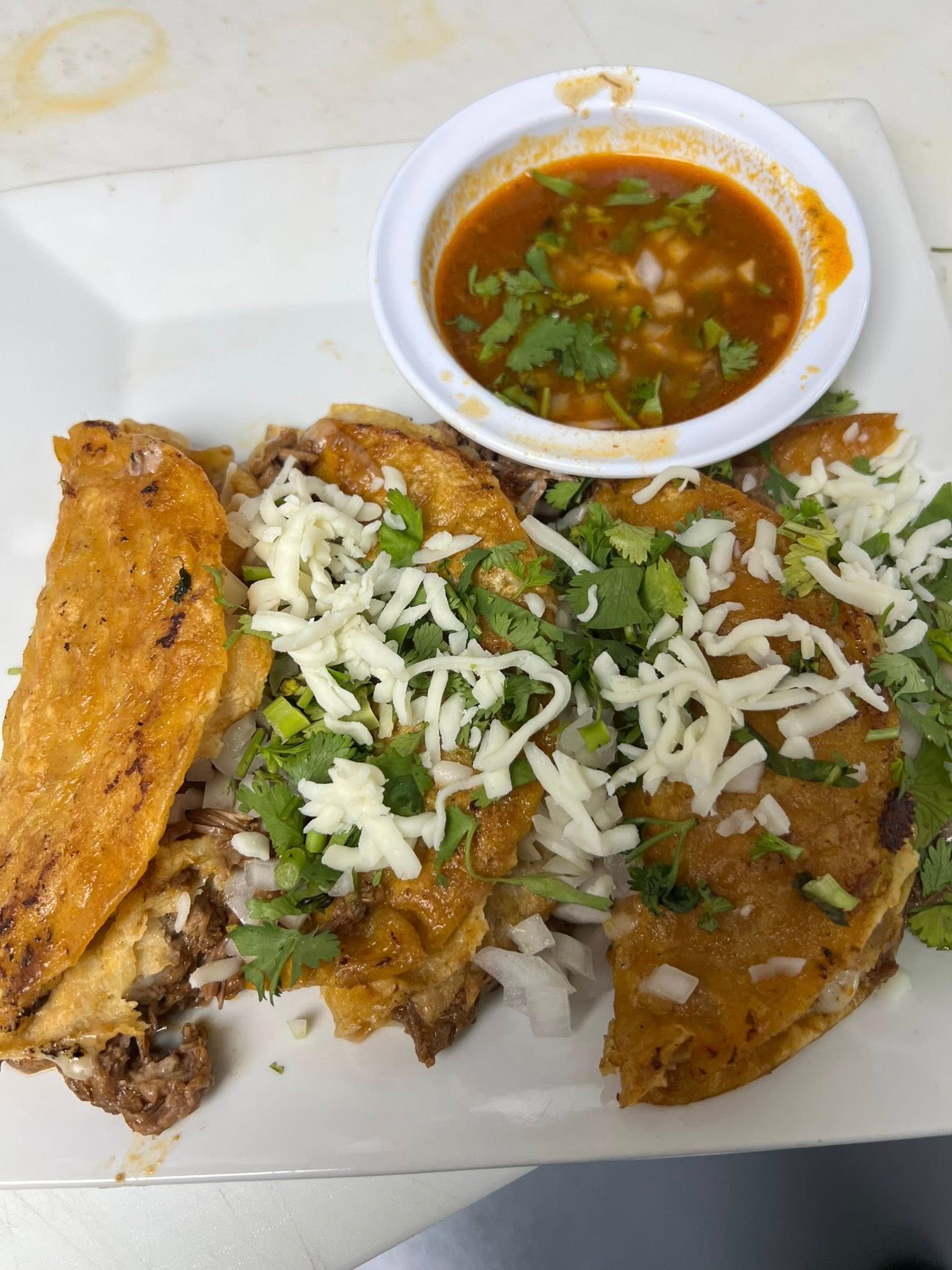 A white plate topped with tacos and a bowl of sauce.