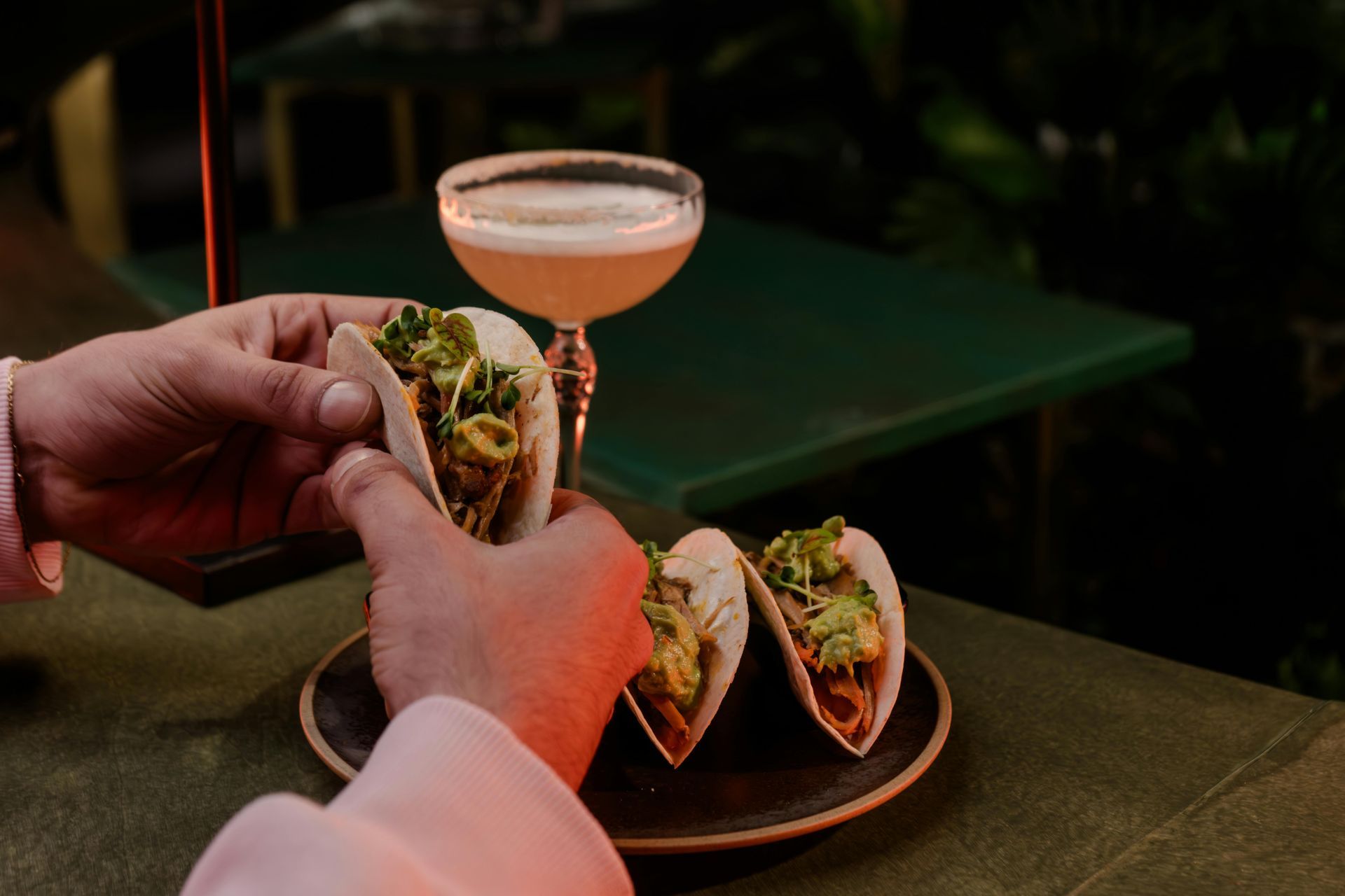 A person is holding a taco next to a martini glass.