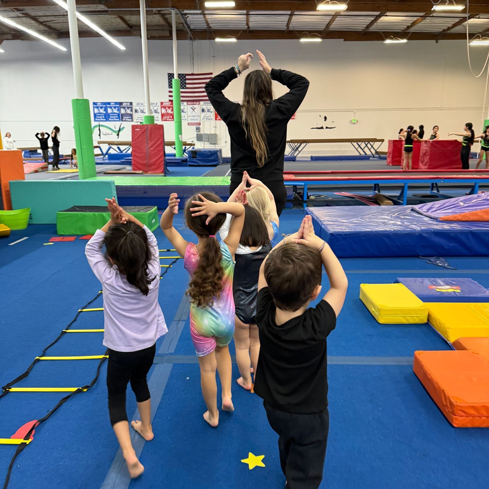 A group of children are standing in a gym with their hands in the air.