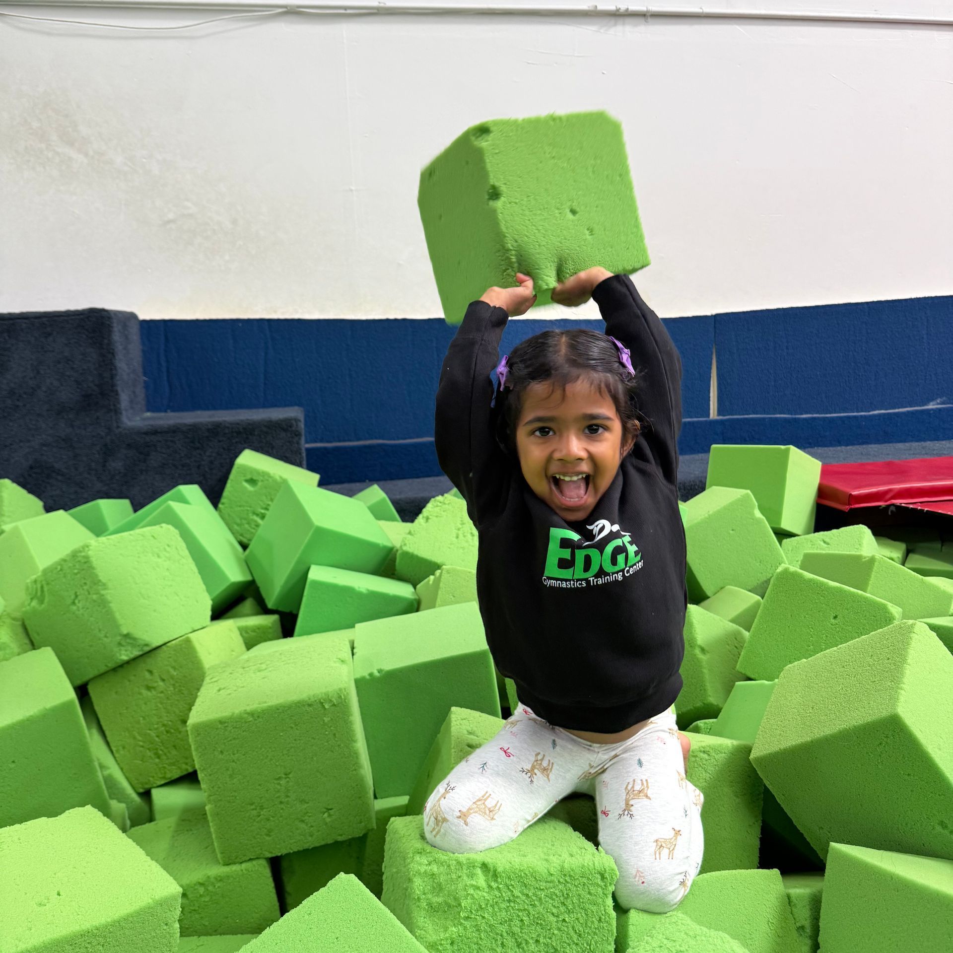 A little girl is sitting in a pile of green foam cubes