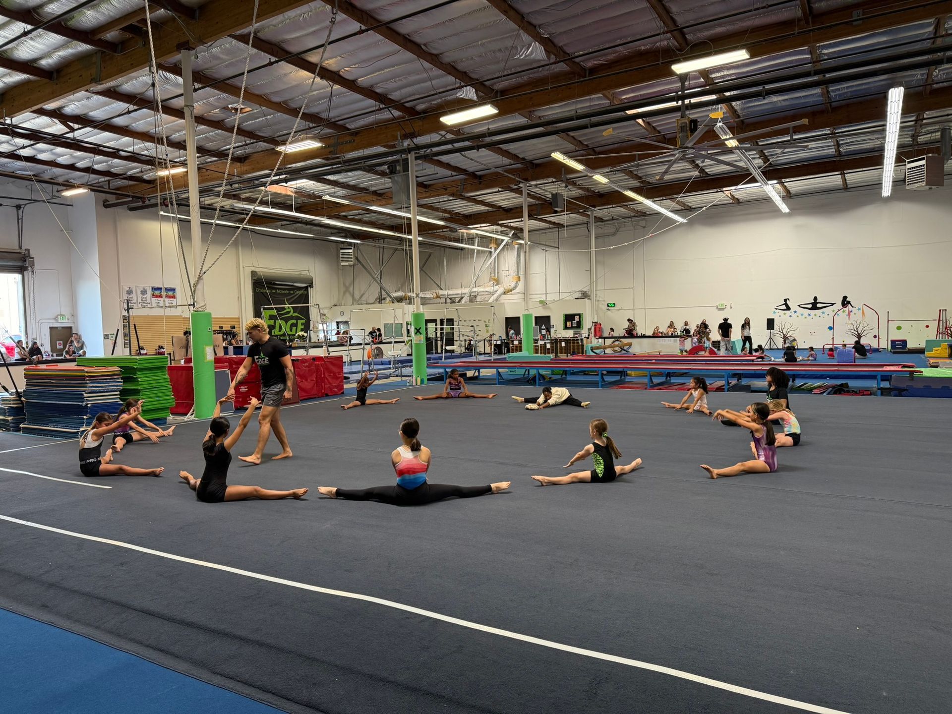 A group of young girls are doing splits on a gym floor.