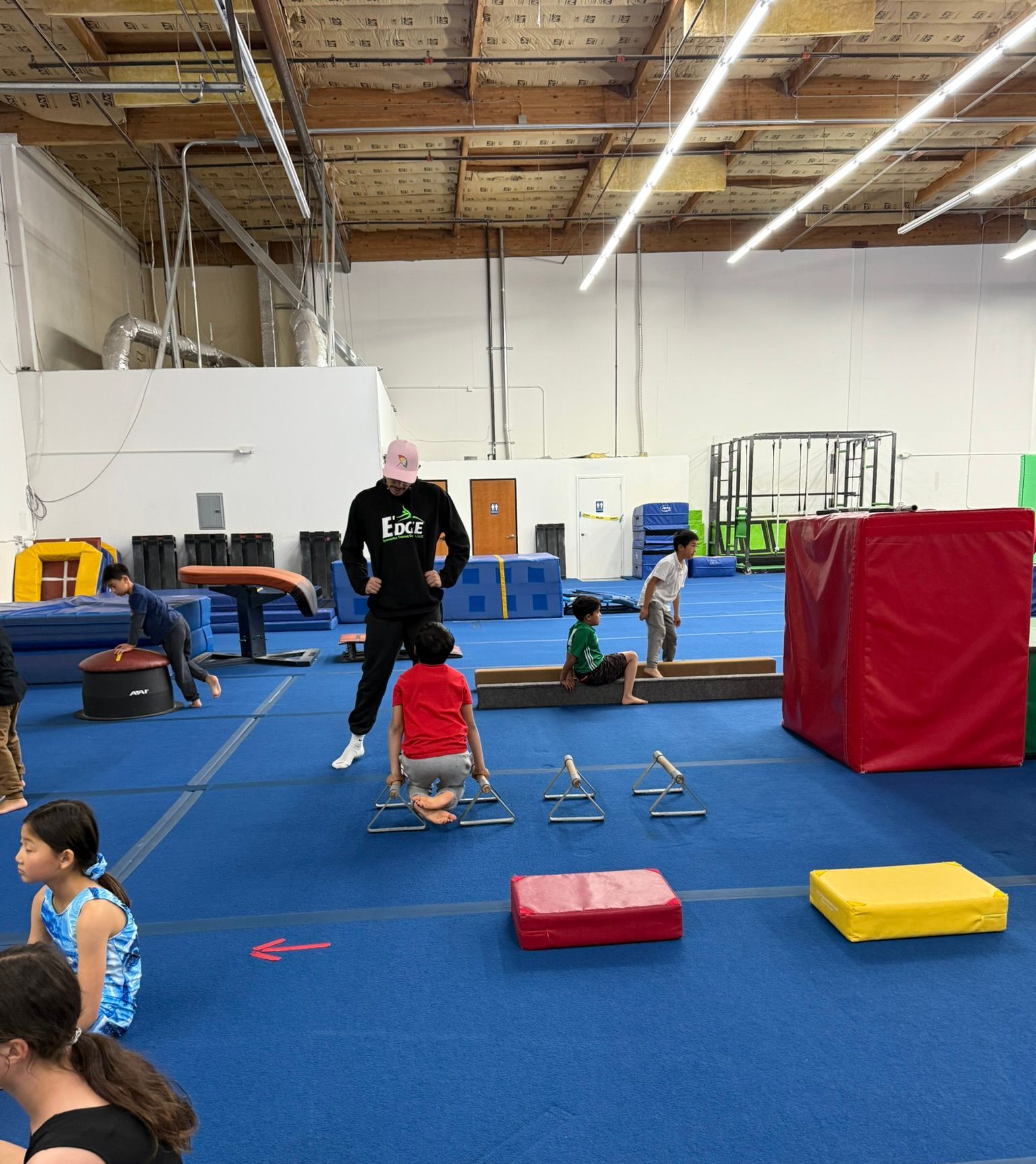 A group of children are playing in a gym with a man wearing a shirt that says ' i love you ' on it