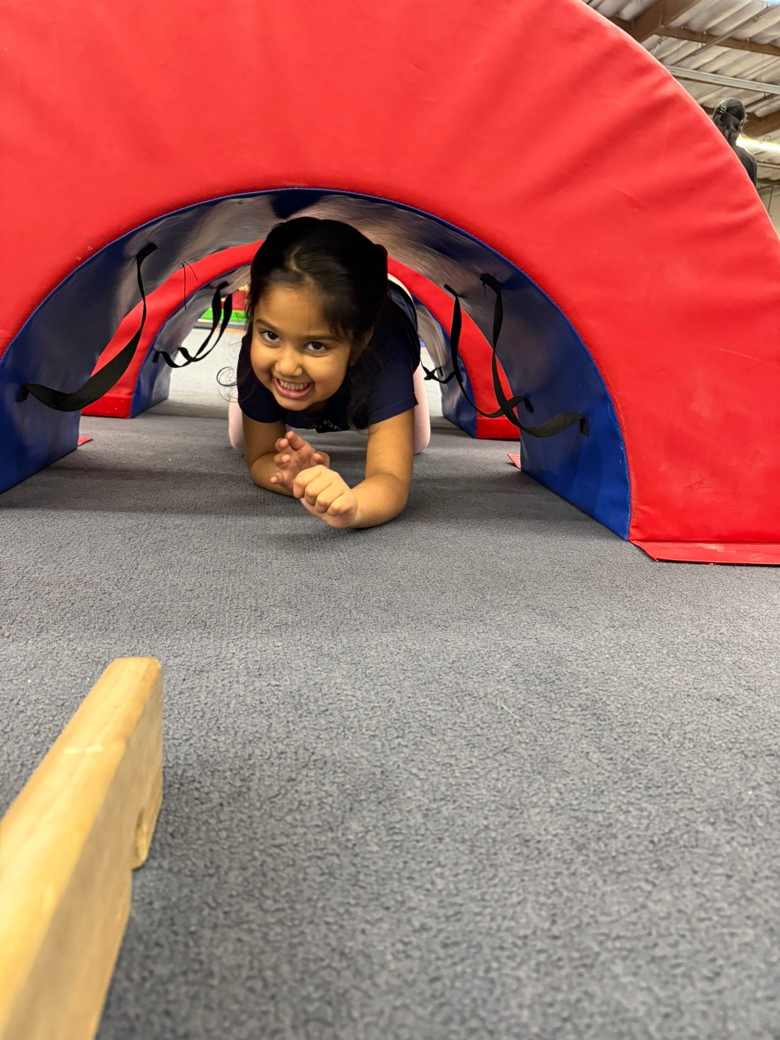 A little girl is crawling through a tunnel in a gym.