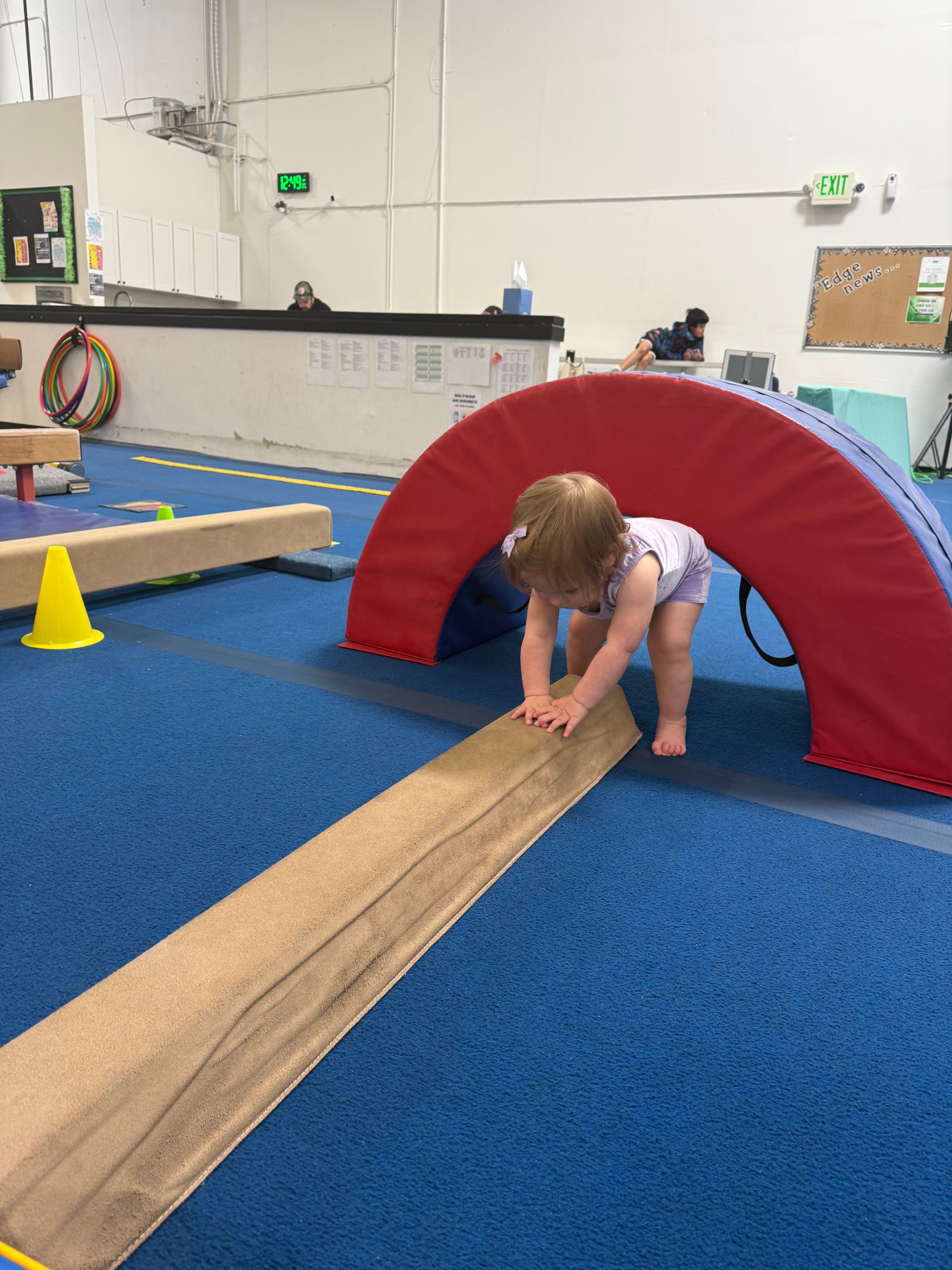 A little girl is crawling on a balance beam in a gym