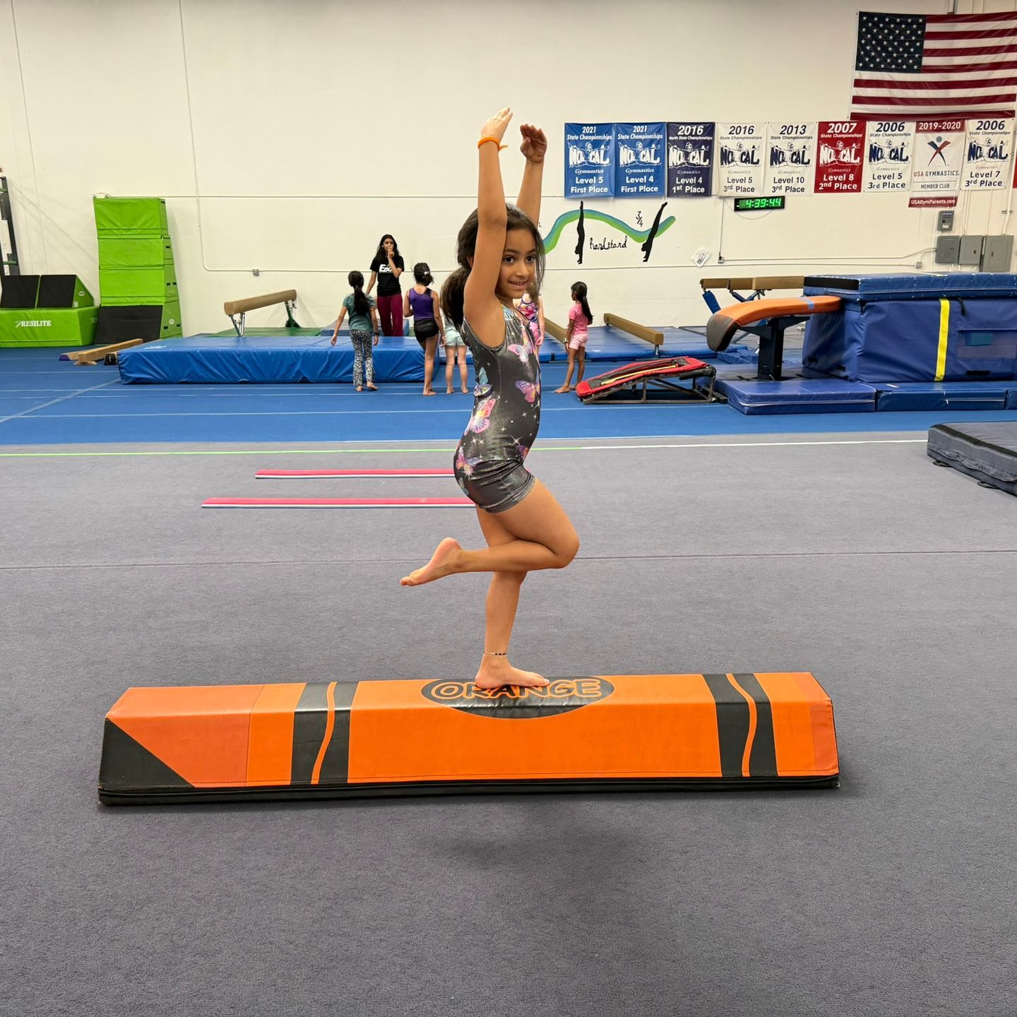A little girl is standing on one leg on a balance beam
