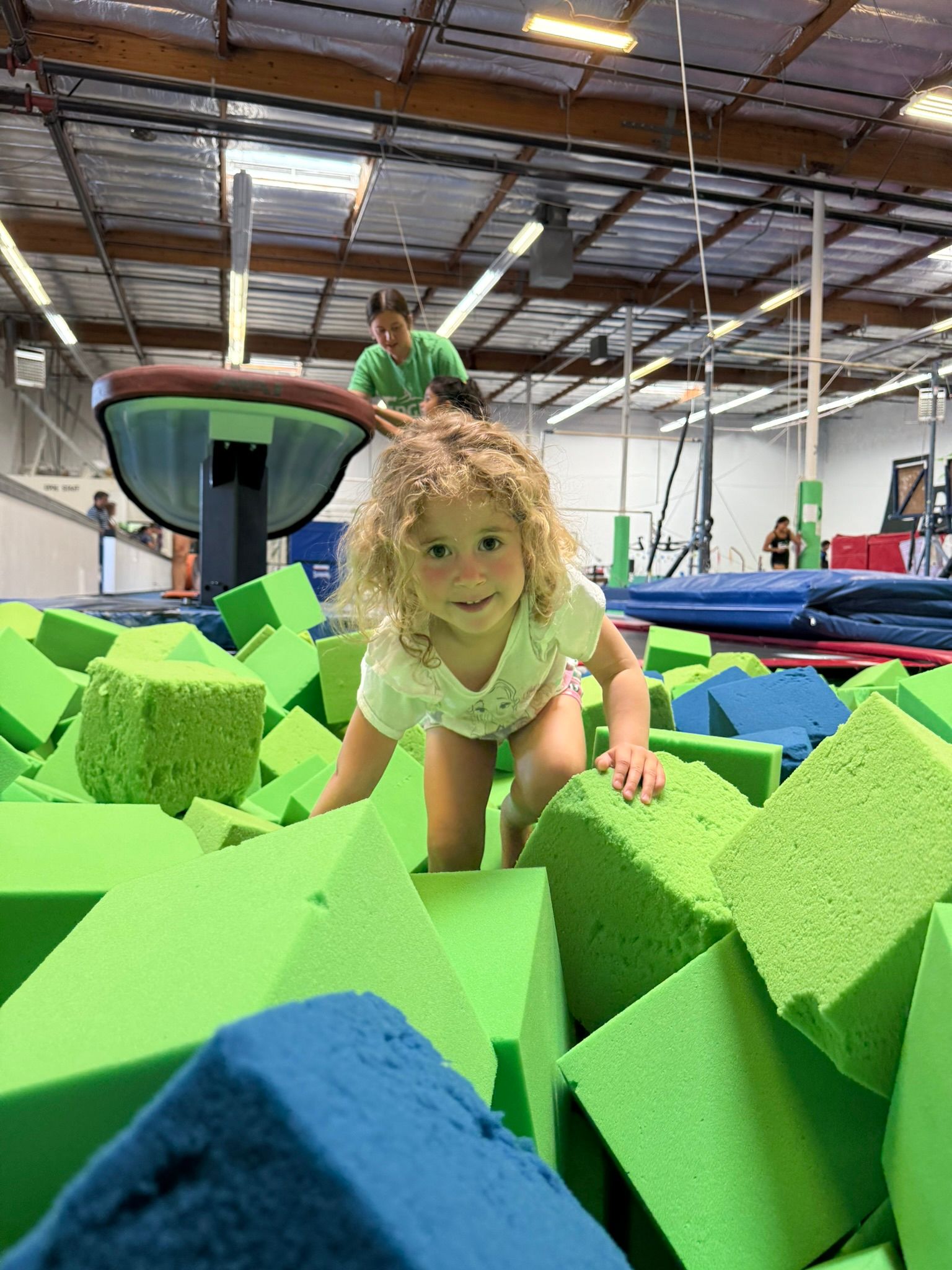 A little girl is crawling through a pile of green and blue foam blocks.