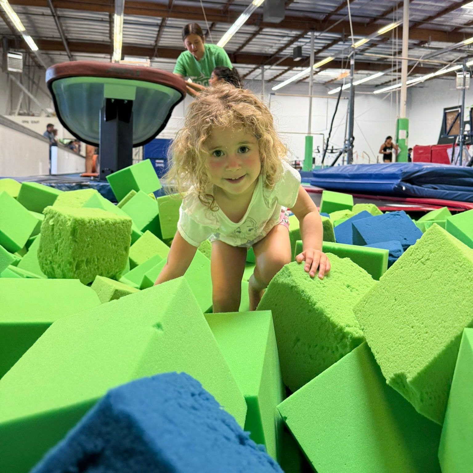 A little girl is crawling through a pile of green and blue foam blocks