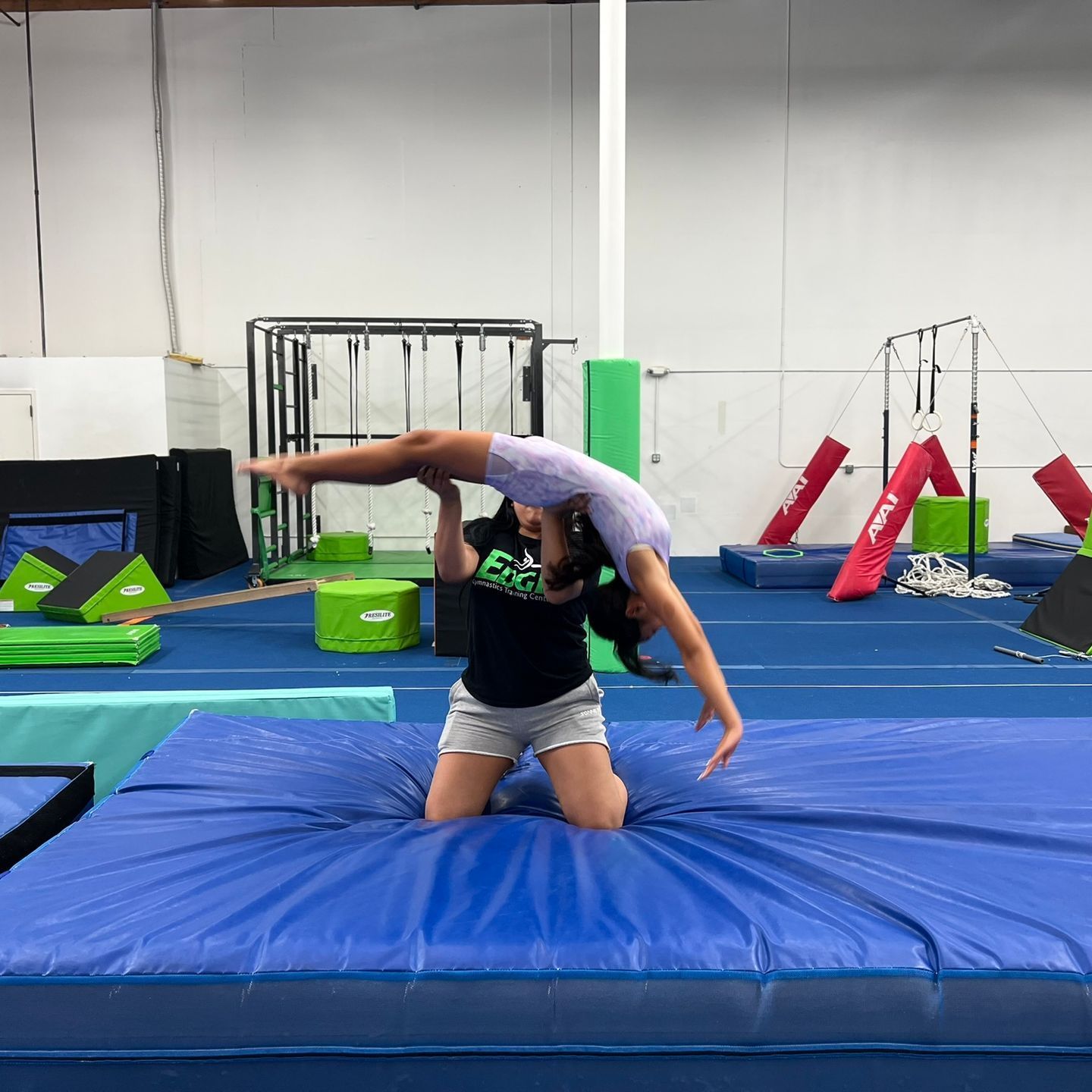 A woman is doing a handstand on a blue mat in a gym.