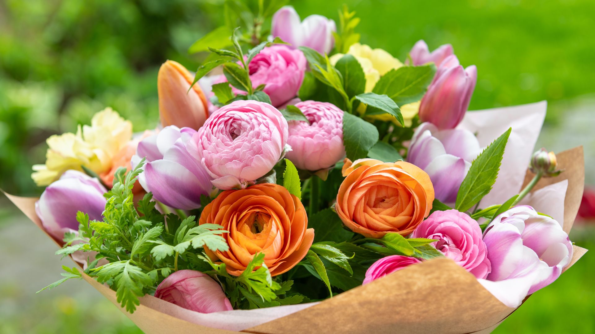 Bouquet of pink, orange, and yellow flowers wrapped in brown paper