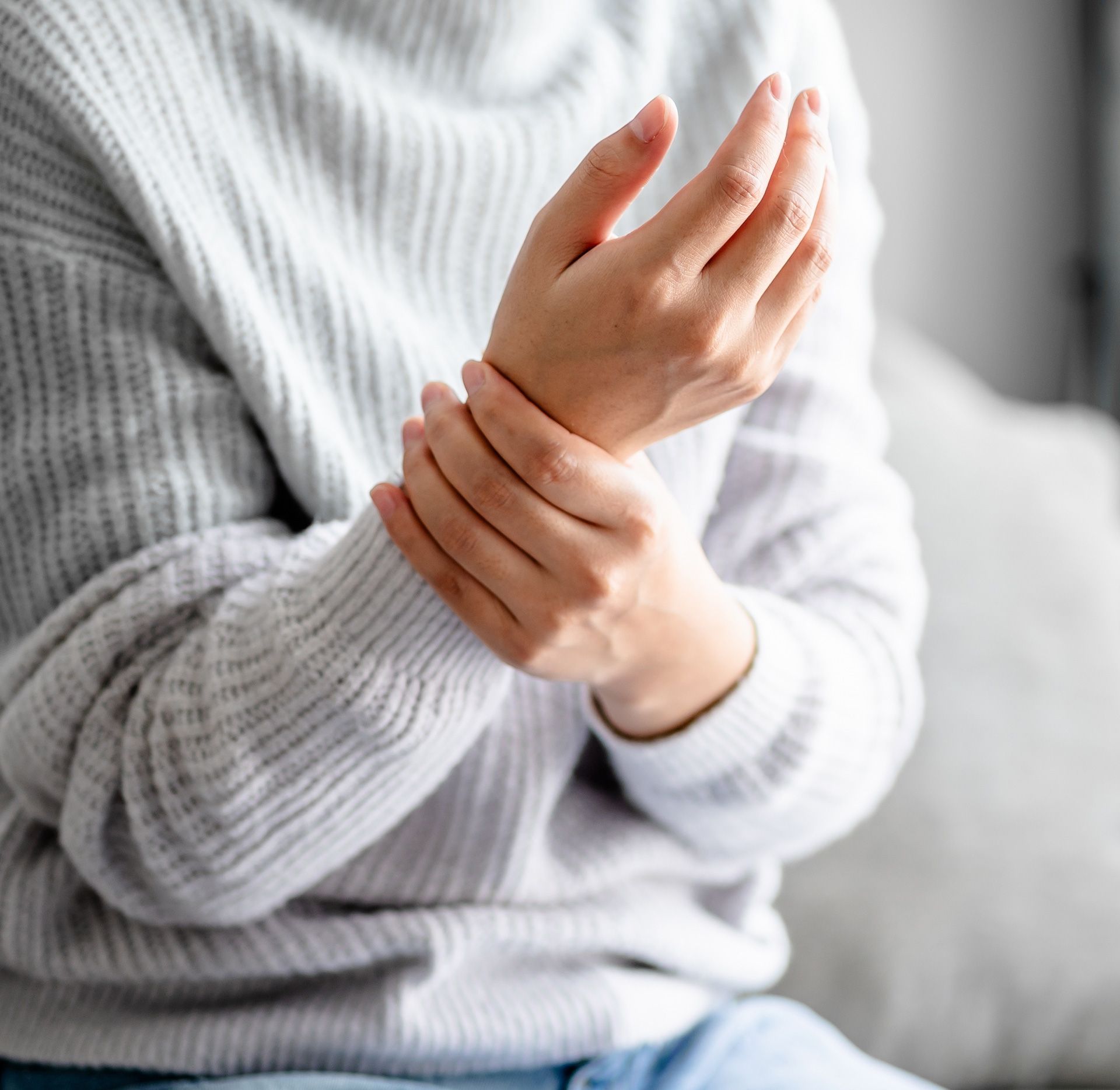 Person holding their left wrist, likely in pain, indoors.