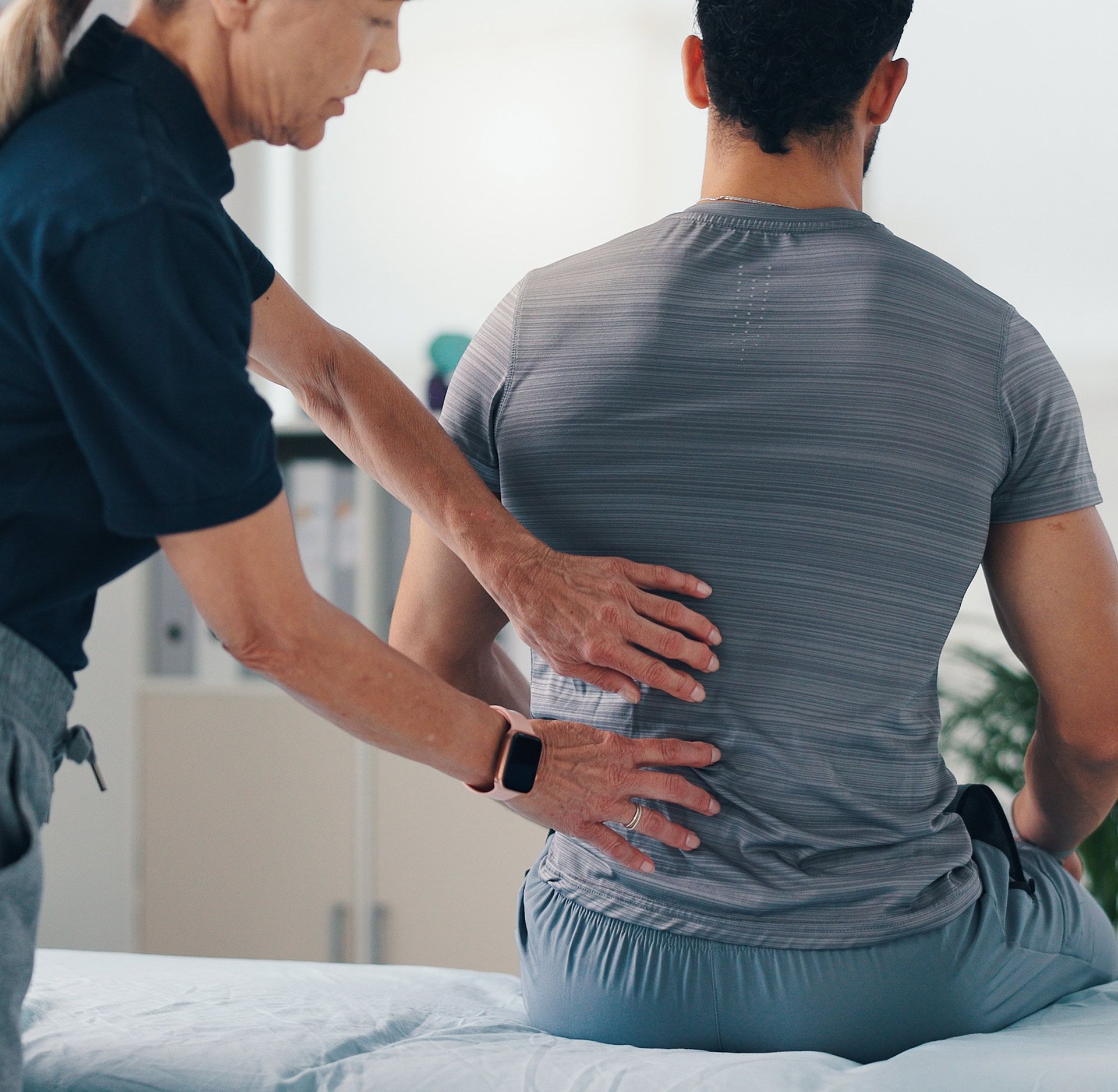 Woman's hands on a person's lower back during an examination in a medical setting.
