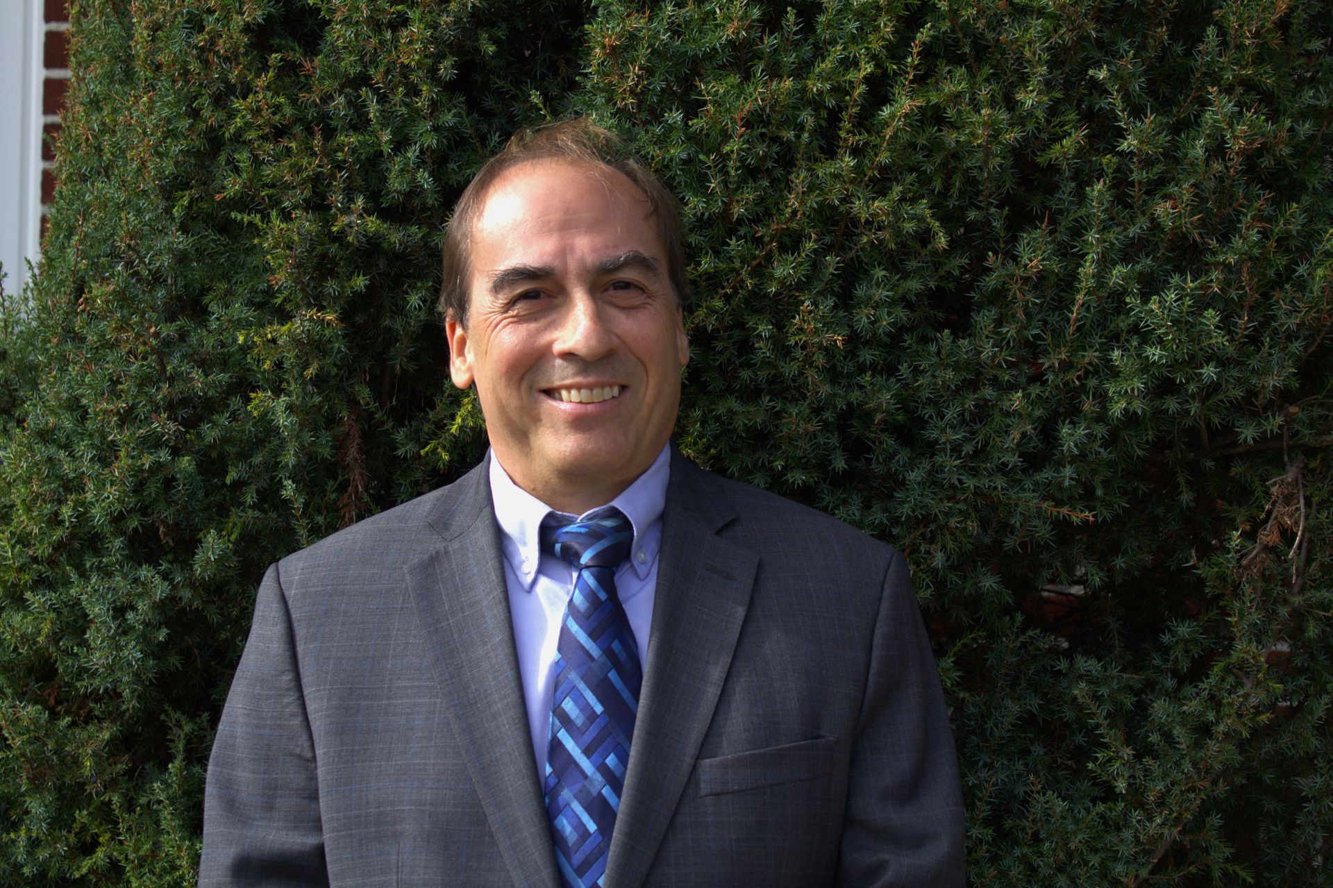 A man in a suit and tie is standing in front of a bush.