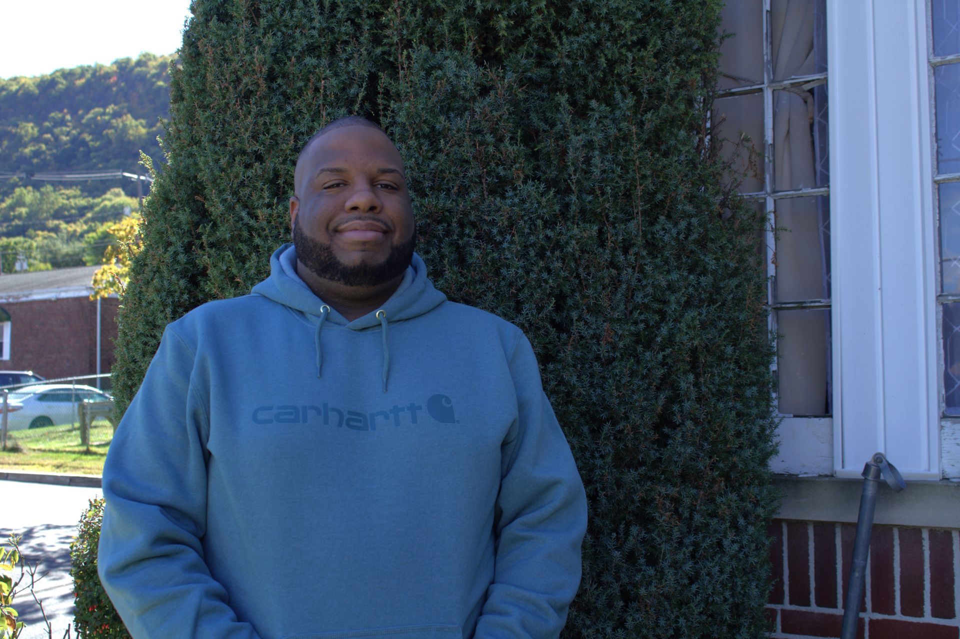 A man wearing a carhartt hoodie is standing in front of a bush.