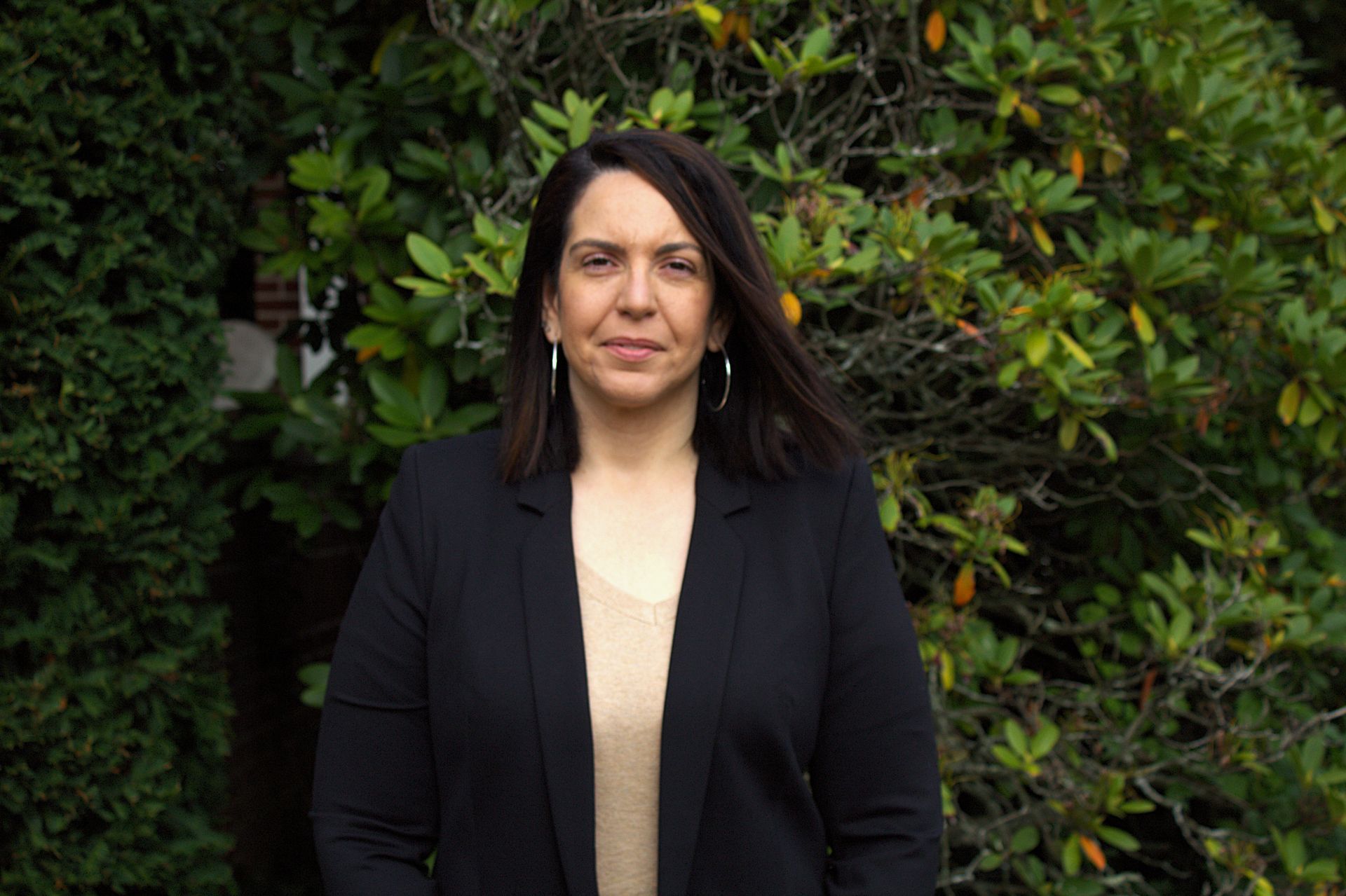 A woman in a black jacket is standing in front of a tree.