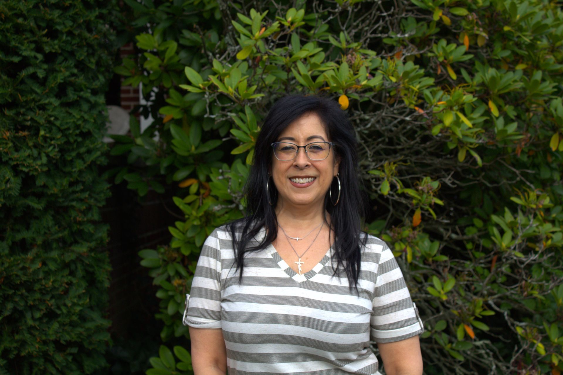 A woman wearing glasses and a striped shirt is standing in front of a tree.
