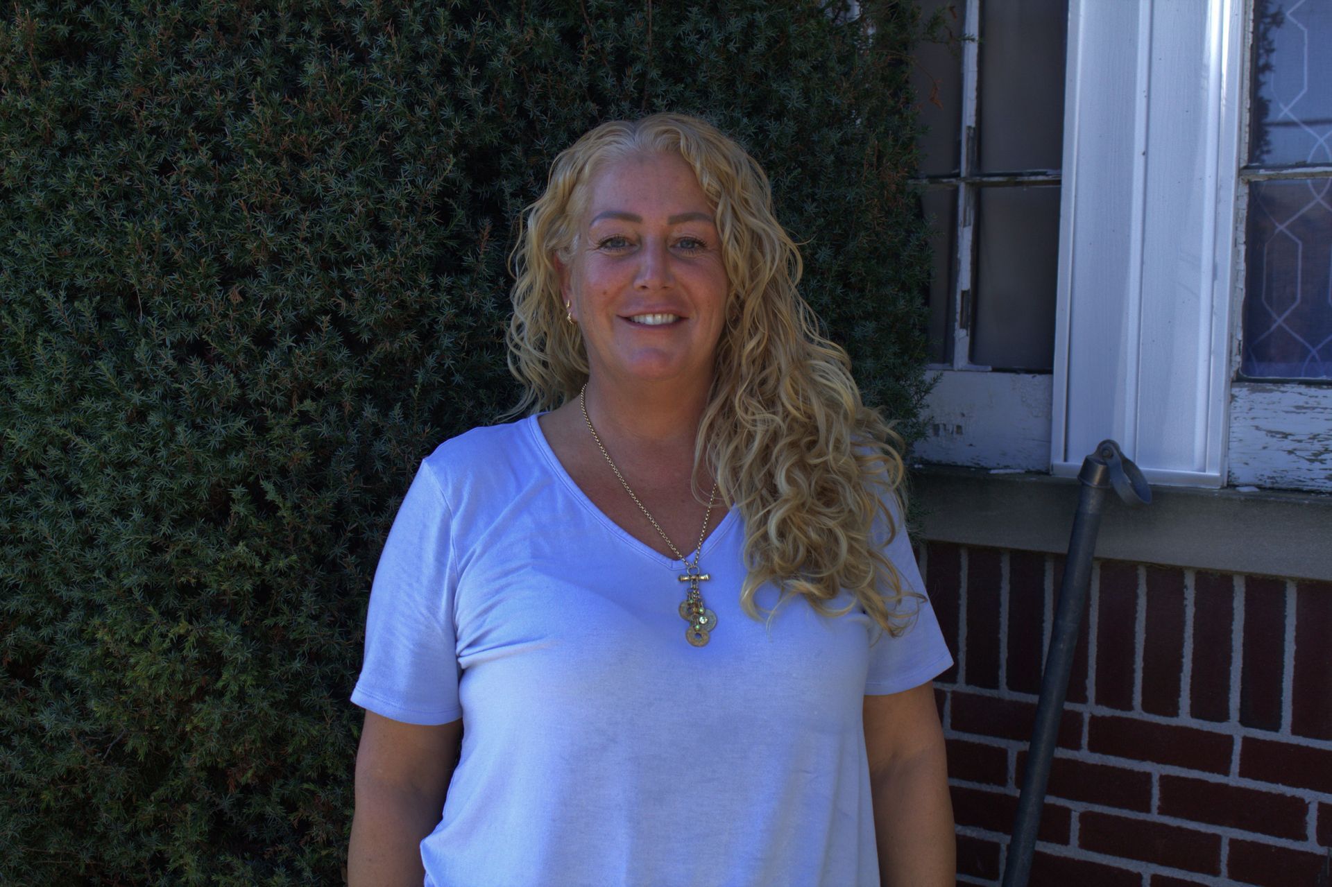 A woman in a white shirt is standing in front of a brick building.