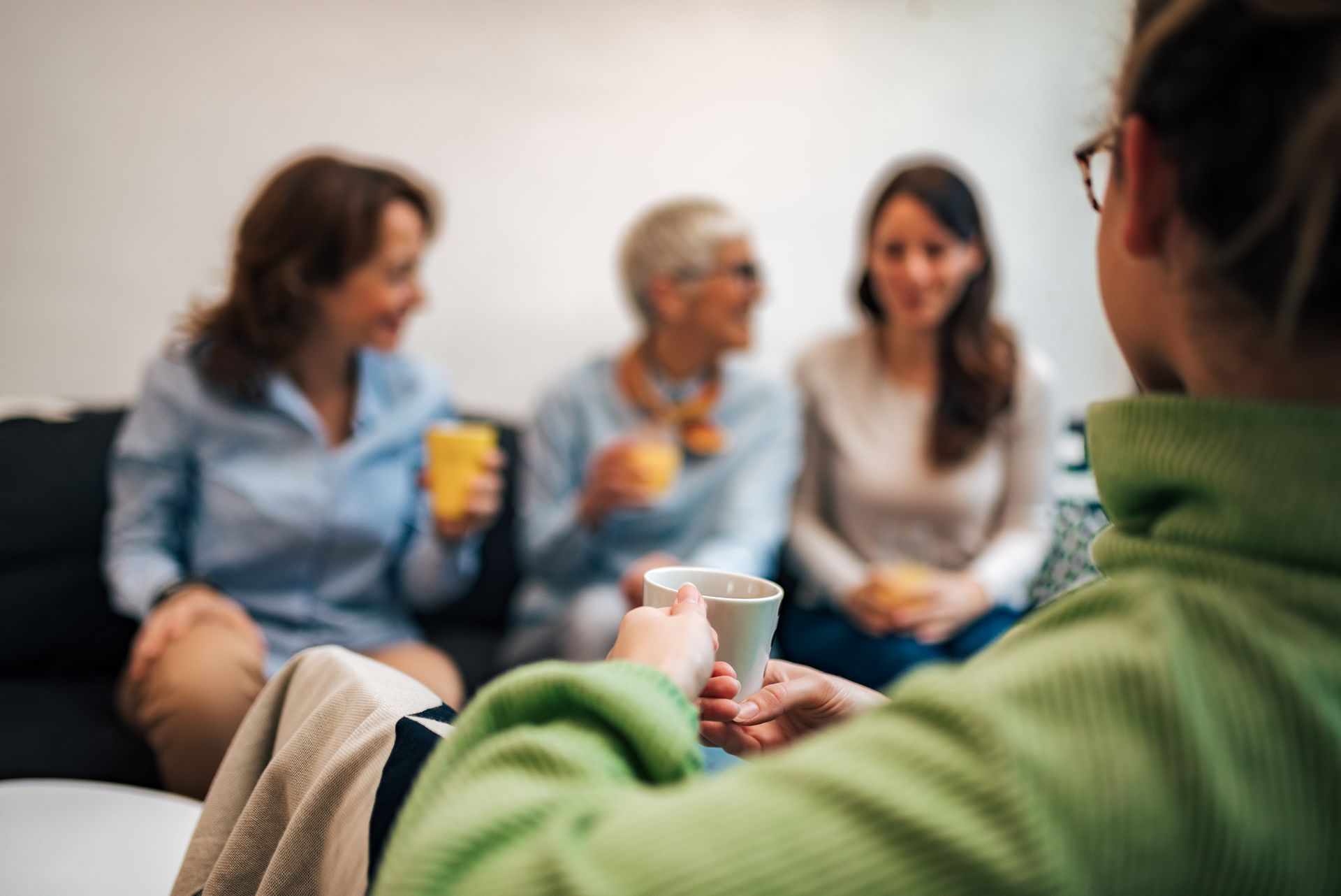 A group of women are sitting on a couch drinking coffee.