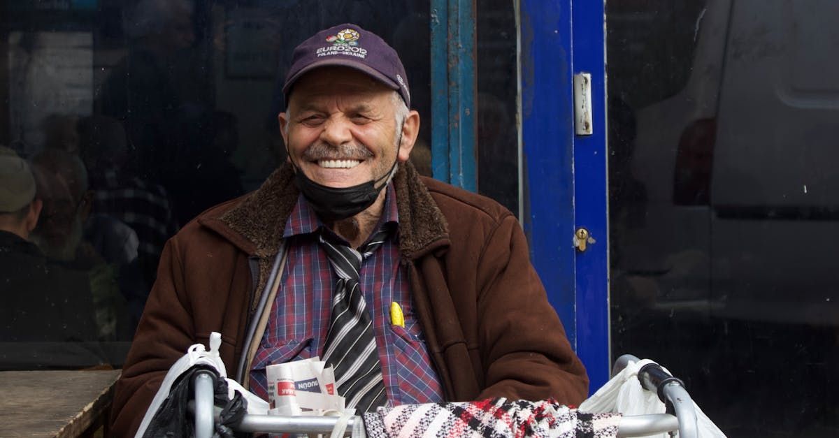 An elderly man wearing a hat and tie is smiling while sitting in front of a blue door.