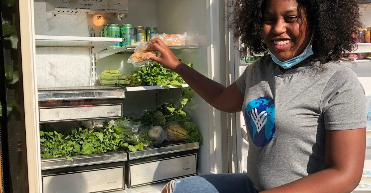 A woman is sitting in front of a refrigerator filled with vegetables.