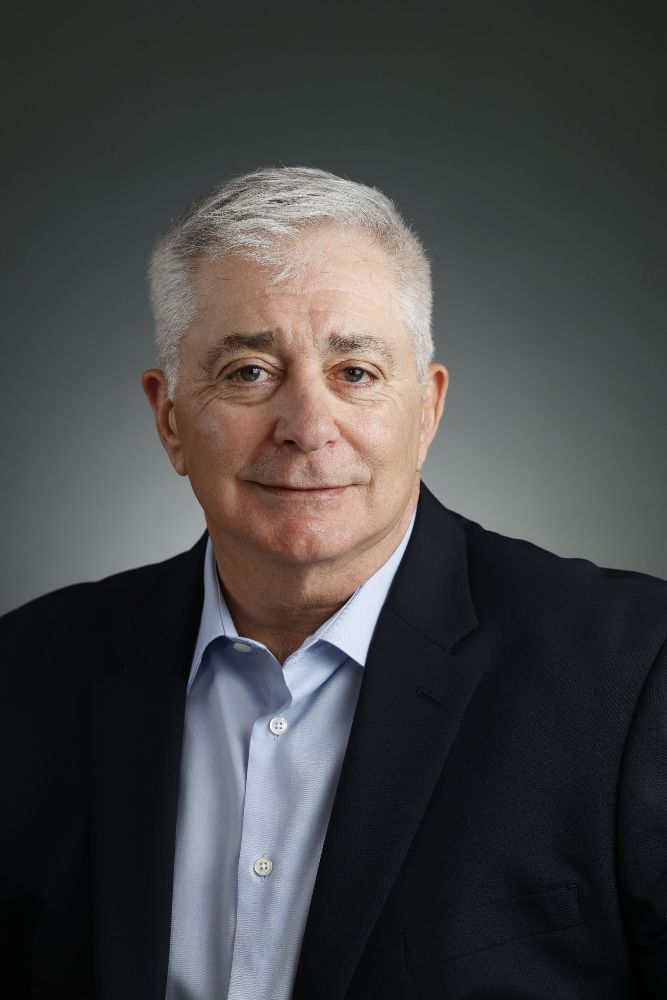 A man in a suit and blue shirt is smiling for the camera.
