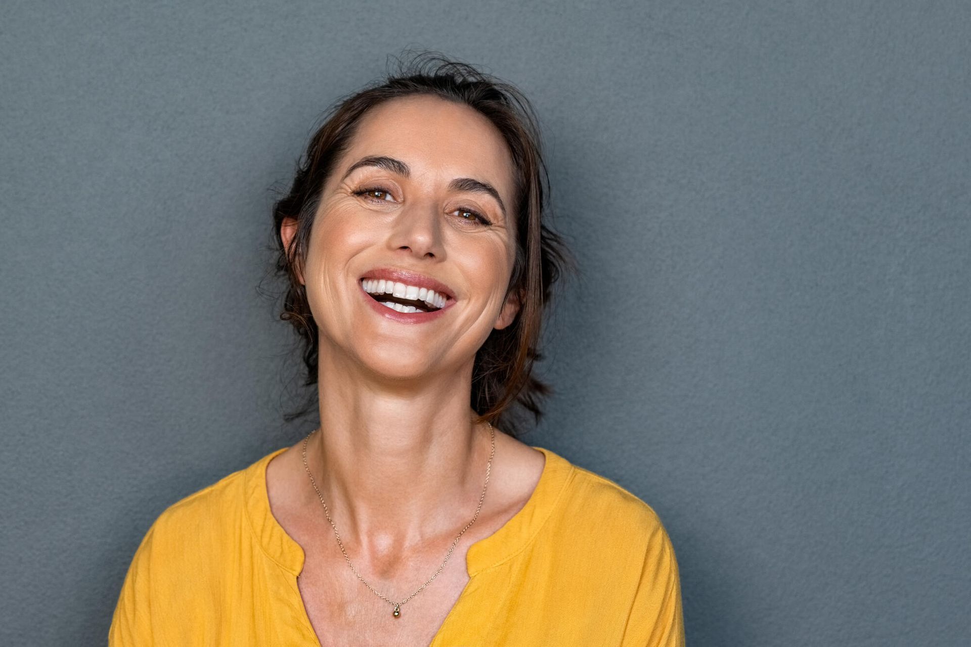 A woman in a yellow shirt is smiling and looking at the camera.