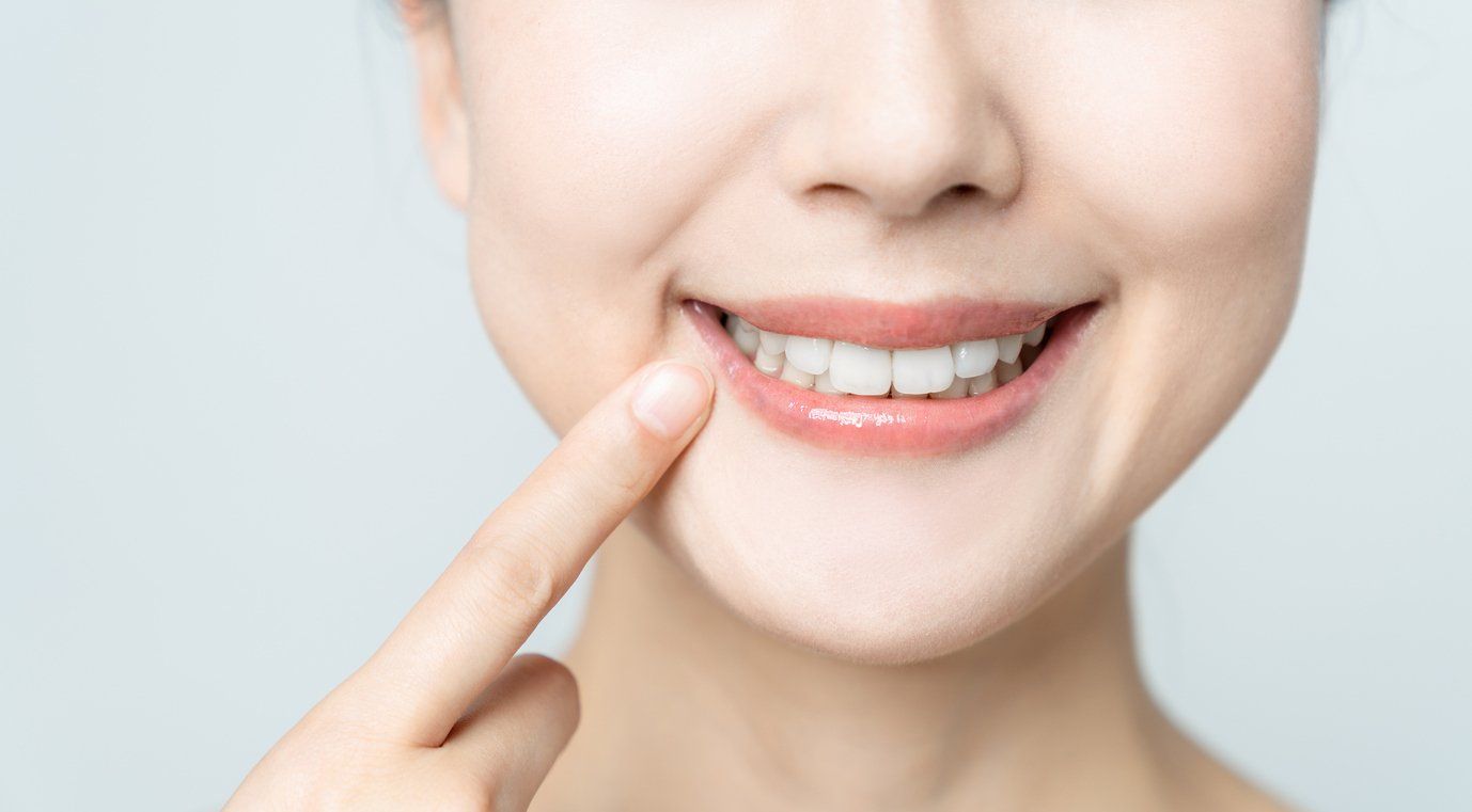 A woman is pointing at her teeth with her finger.