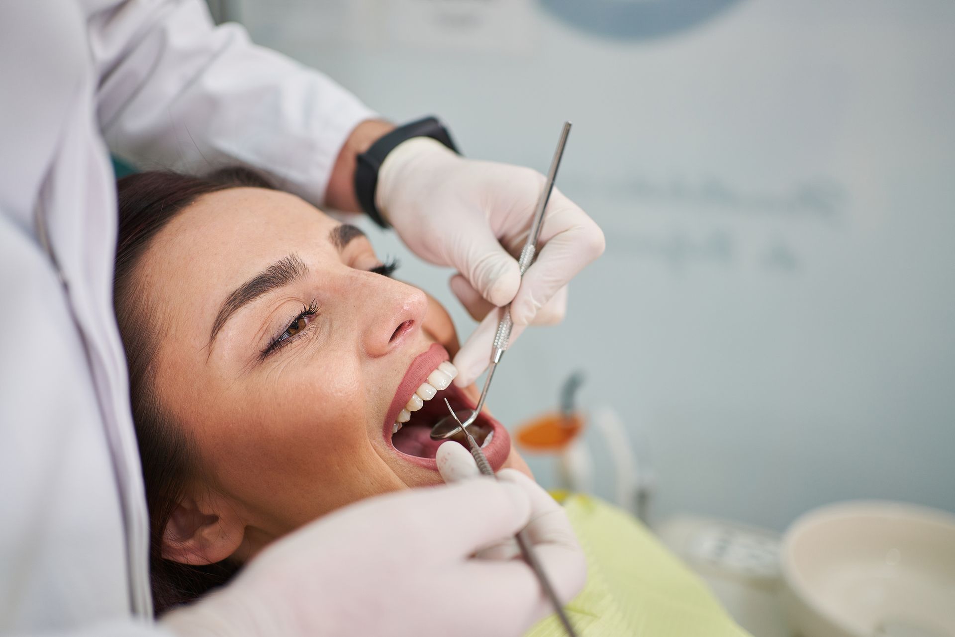 Dentist examining a woman's teeth with instruments. Woman's mouth is open, in a dental office setting.