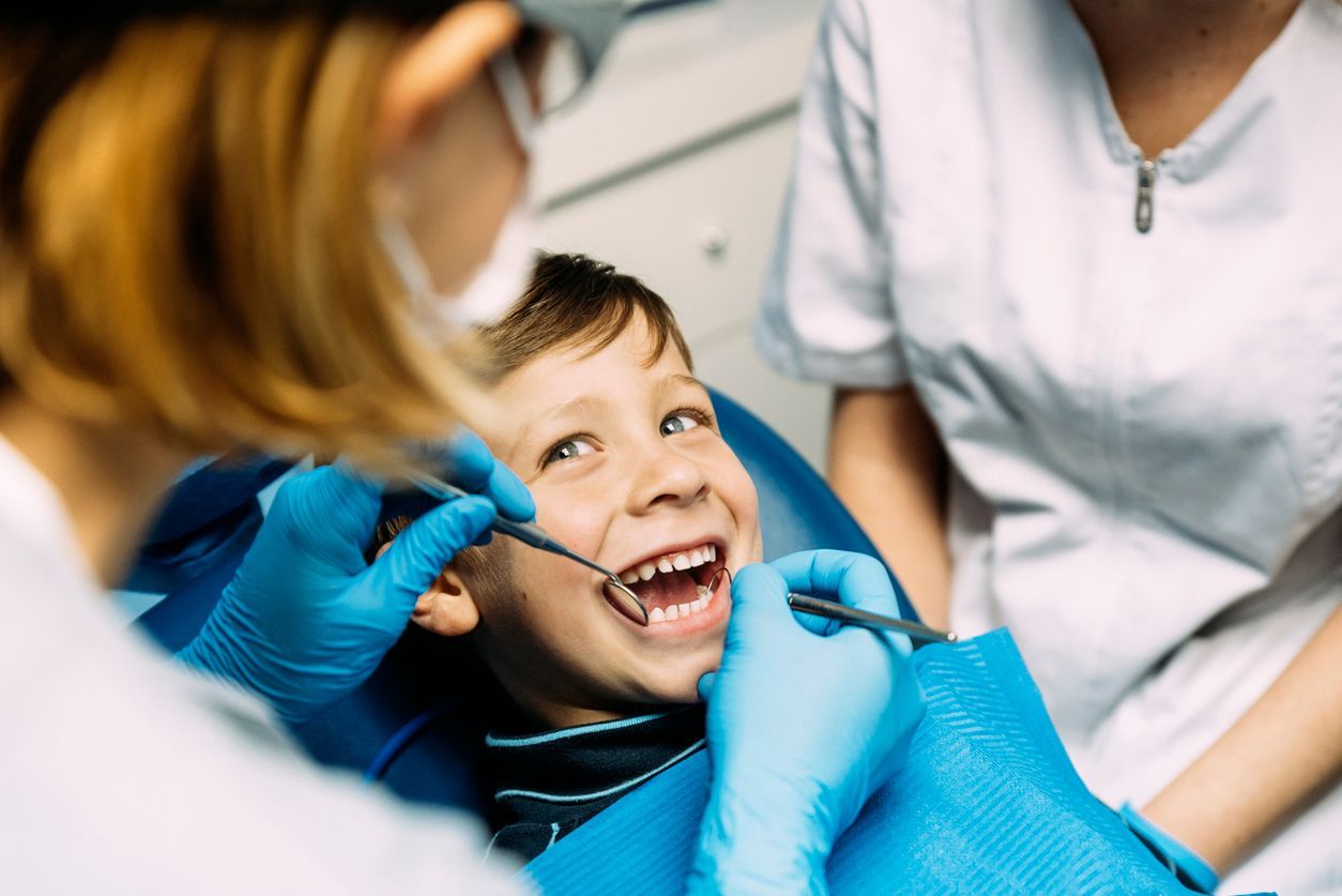 Boy smiling at dentist during checkup; dentist and assistant in blue gloves.