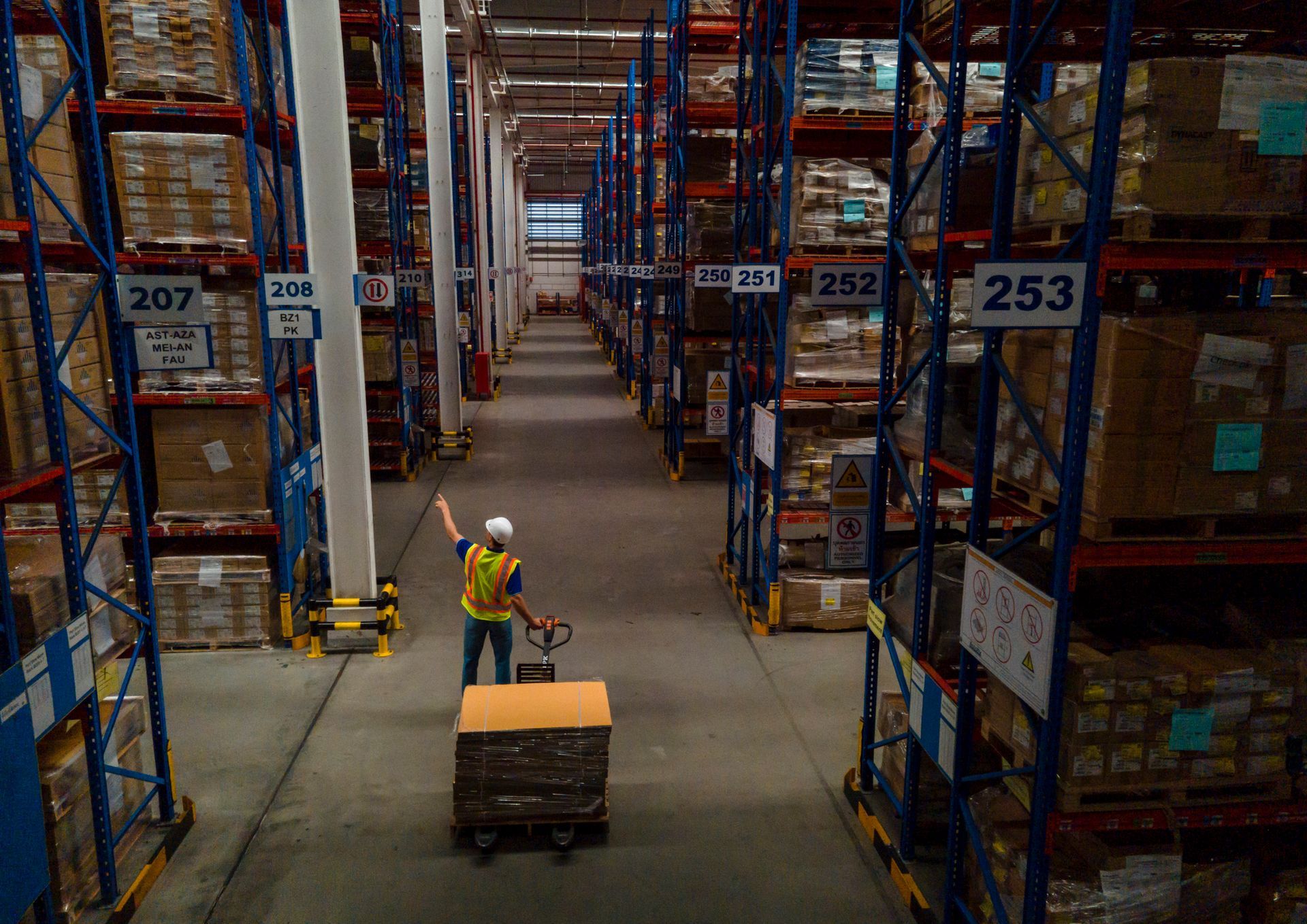 A warehouse worker pulls a pallet with boxes, inside a warehouse.