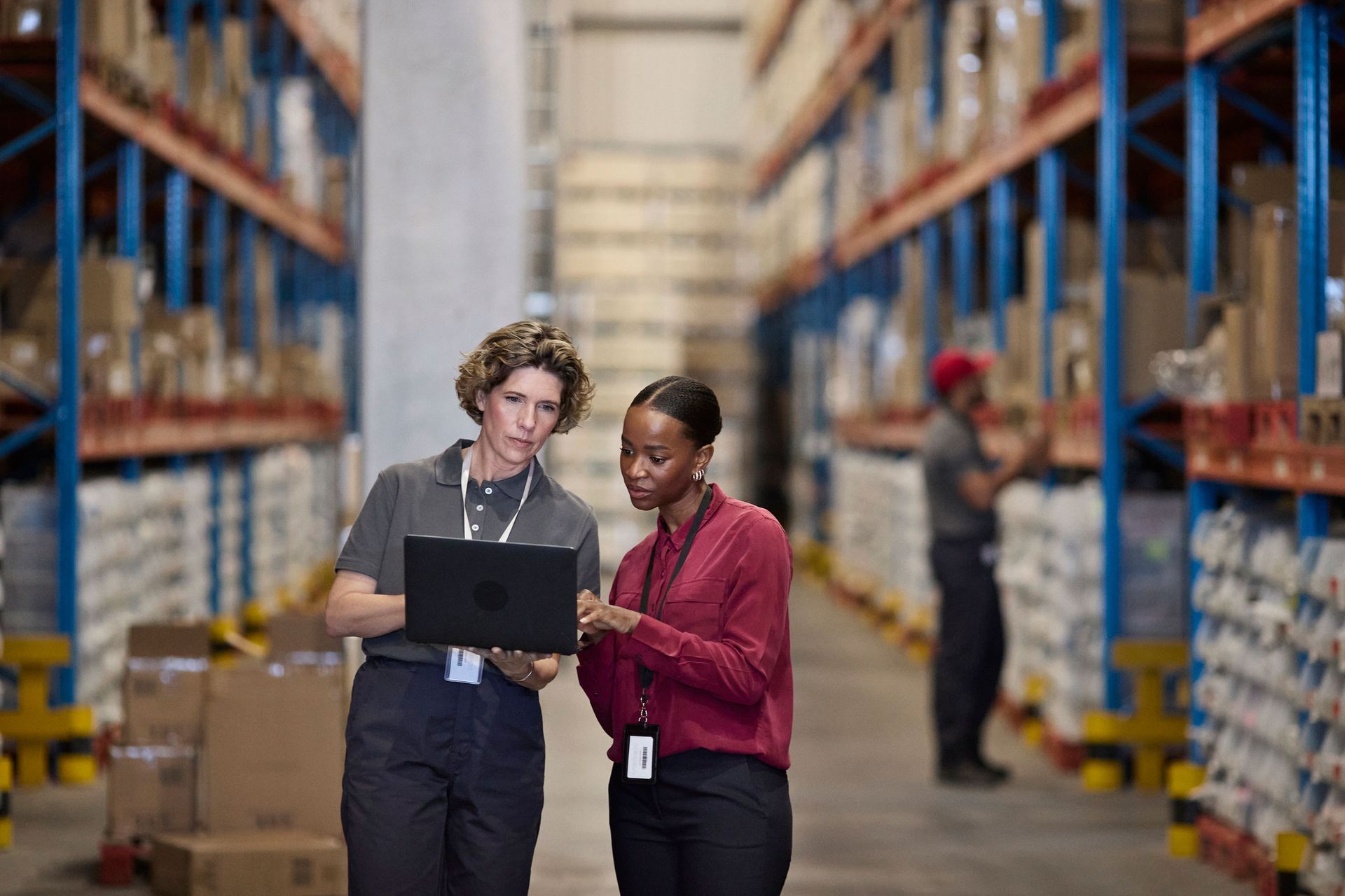 Two female managers check logistic data while standing next to each other. Two female managers check logistic data while standing next to each other.