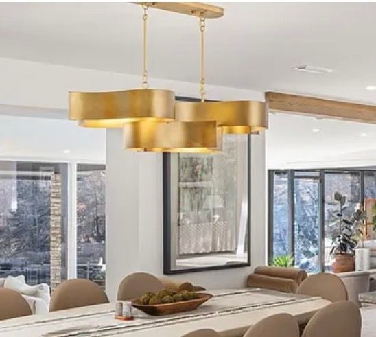 Modern dining room with a gold pendant chandelier above a long table and neutral chairs