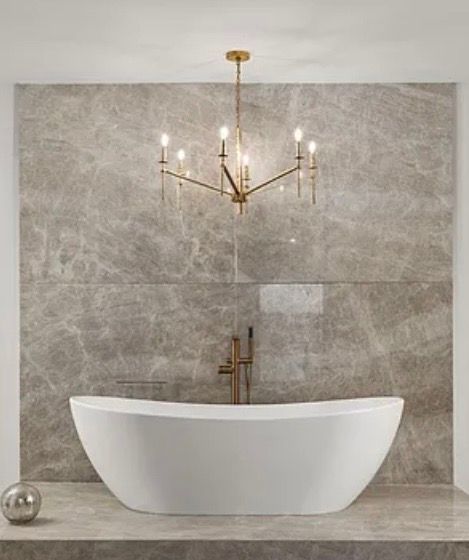 Modern bathroom with freestanding white tub, gray tile wall, and gold chandelier over the faucet
